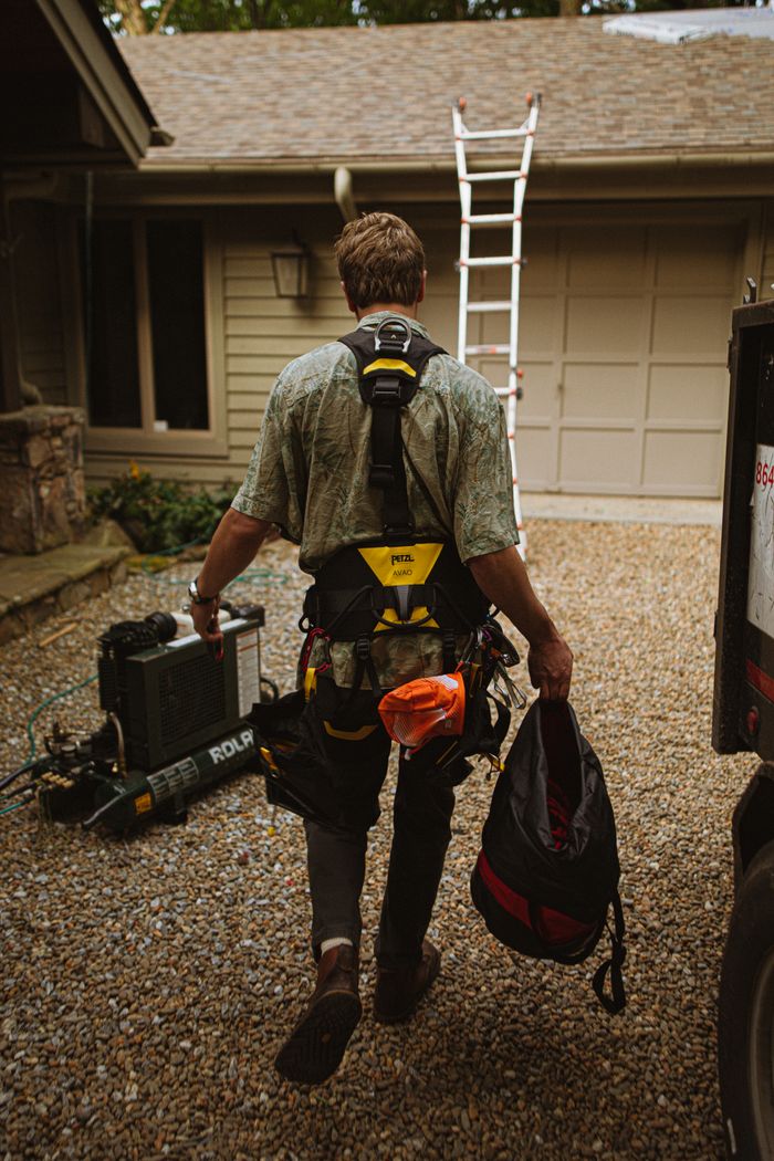 Roofer in safety gear approaches house, ladder ready for roof installation.