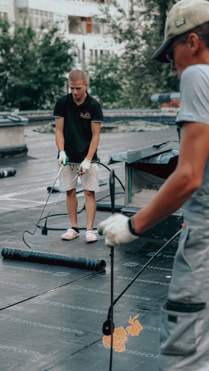 Two workers using blowtorches for roof installation outdoors on a summer day.