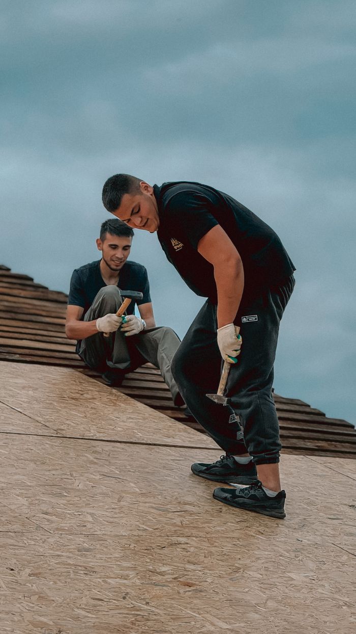 Two men working on a roof installation under a cloudy sky, capturing teamwork and construction action.